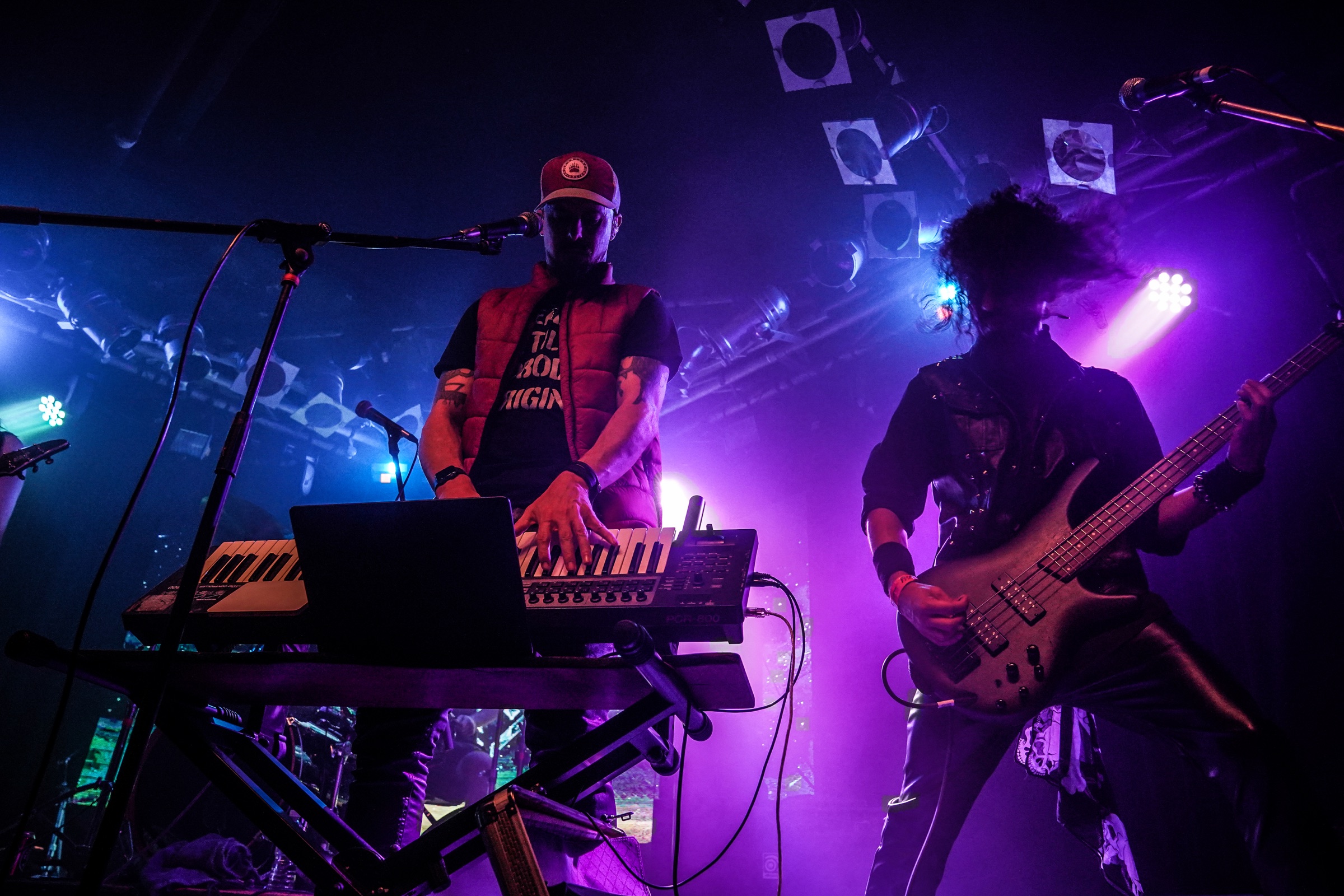 Keyboardist and bassist performing live under blue and purple stage lights